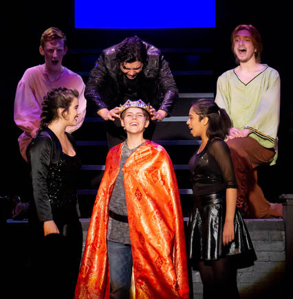 Pippin is crowned. He smiles brightly. We view him from the audience, as he is surrounded by other actors.