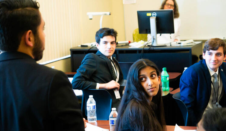 A class of students look up at a speaker. The viewer is looking over the speaker's shoulder at them.