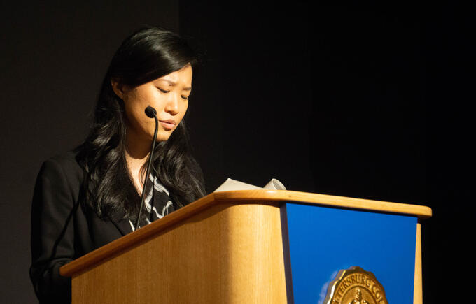 Jenny Xie, author, does a live reading of her book. She sits to the left, behind a podium, with a focused and earnest expression.