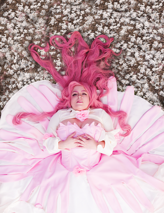 A cosplayer laying on the ground, spread out, in bright pink and white.