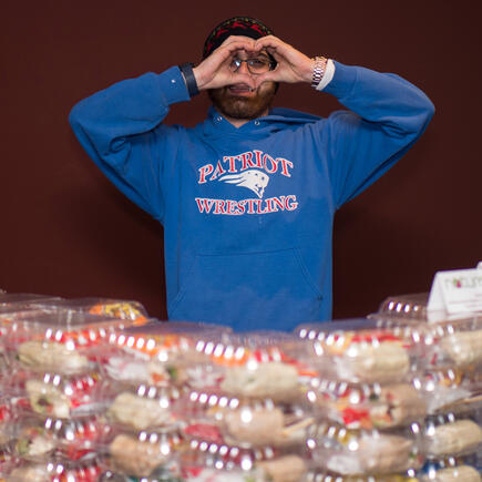 A student making a heart sign at the camera, framed by an endless array of cookies.